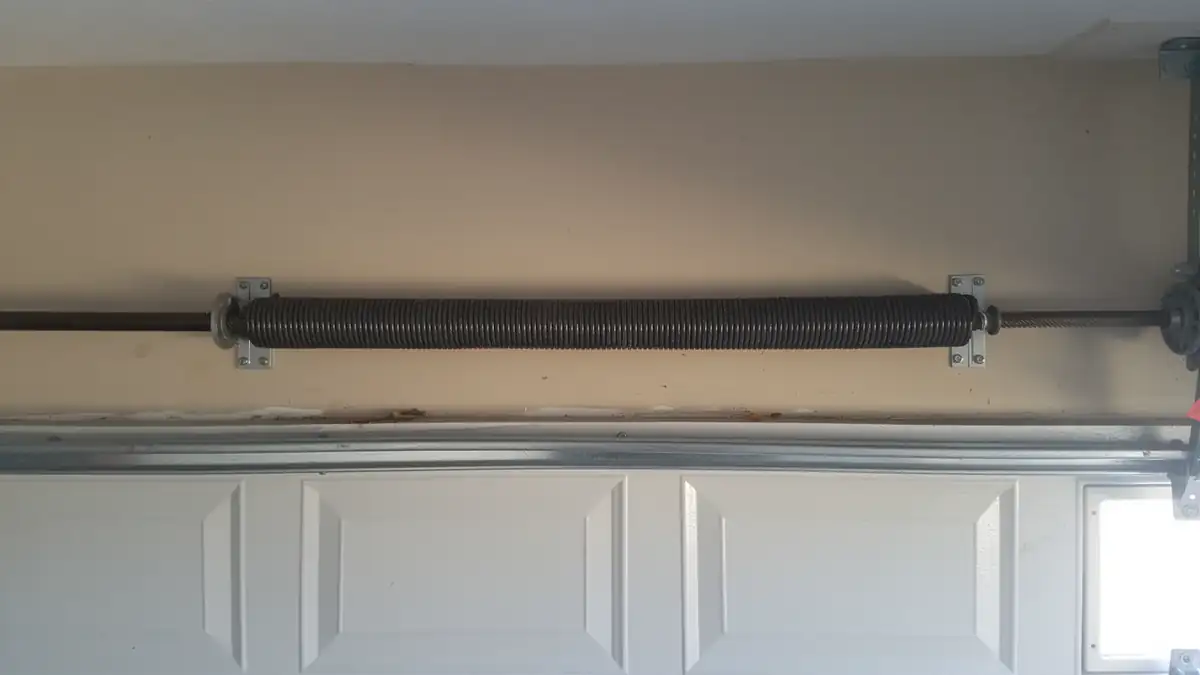 A black torsion spring is mounted above a white garage door.